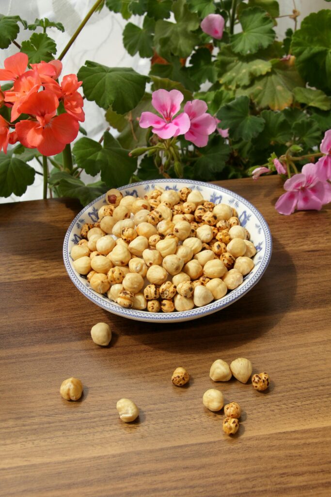 Bowl of dry chickpeas on wooden table surrounded by colorful flowers.