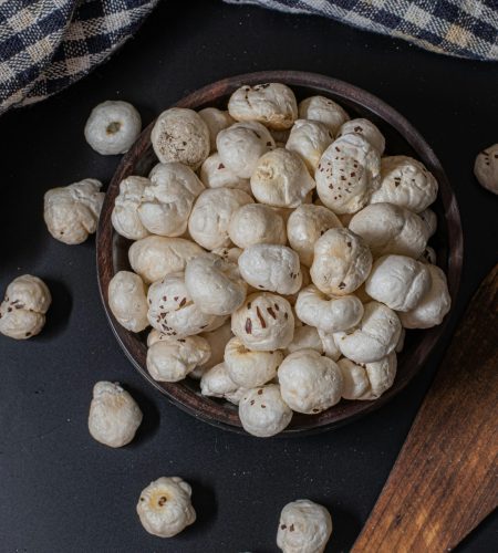 A rustic bowl filled with puffed lotus seeds on a black background, perfect for snacks.